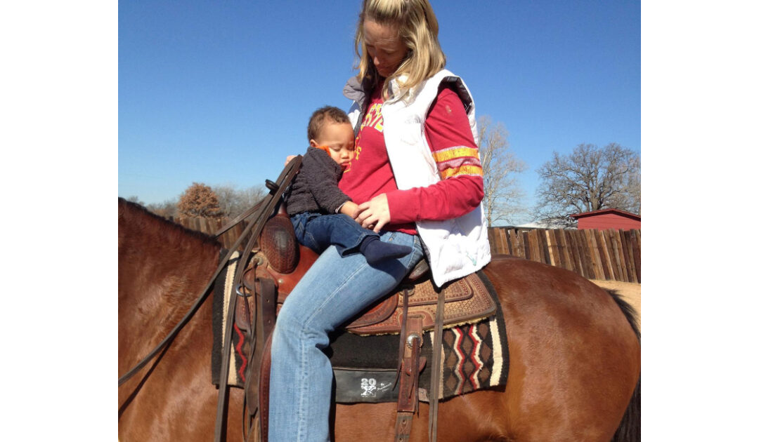 woman in red shirt holding baby while riding horse